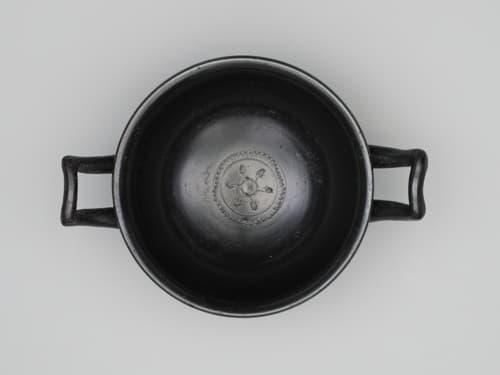 A wide-mouthed drinking cup glazed in black with two handles extending from opposite sides.