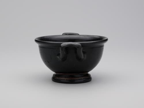 A wide-mouthed drinking cup glazed in black with two handles extending from opposite sides.